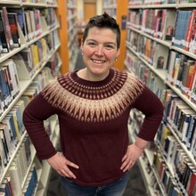 Person standing with hands in hips between library shelves