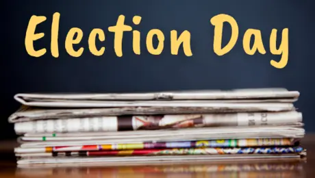 Election day written in yellow on a chalk board over a pile of newspapers