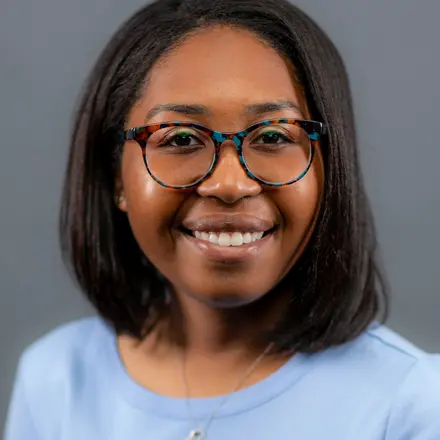 Image of a woman wearing glasses with a grey background.