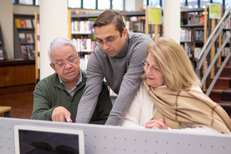 Adobe Stock description says: "Portrait of aged couple getting knowledges. Serious man and woman sitting in library focused on reading books using computer listening to handsome instructor. Education for mature people"