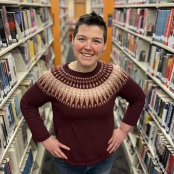 Person standing with hands in hips between library shelves