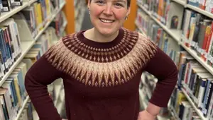 Person standing with hands in hips between library shelves